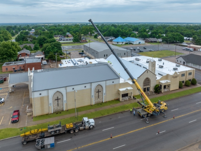 Crane lifting HVAC unit onto metal roof