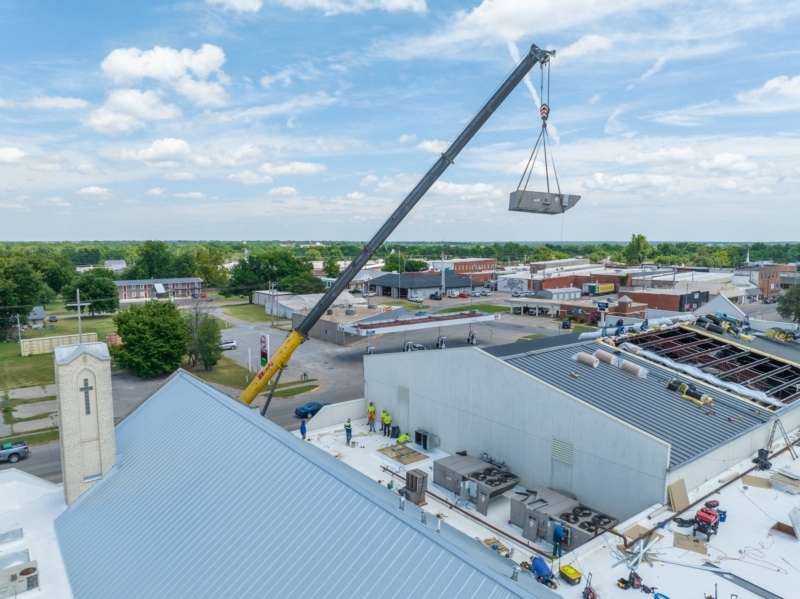 Crane lifting HVAC unit onto metal roof
