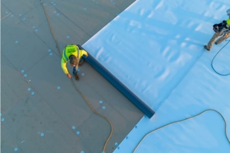 TPO installation showing a roofer rolling out the material