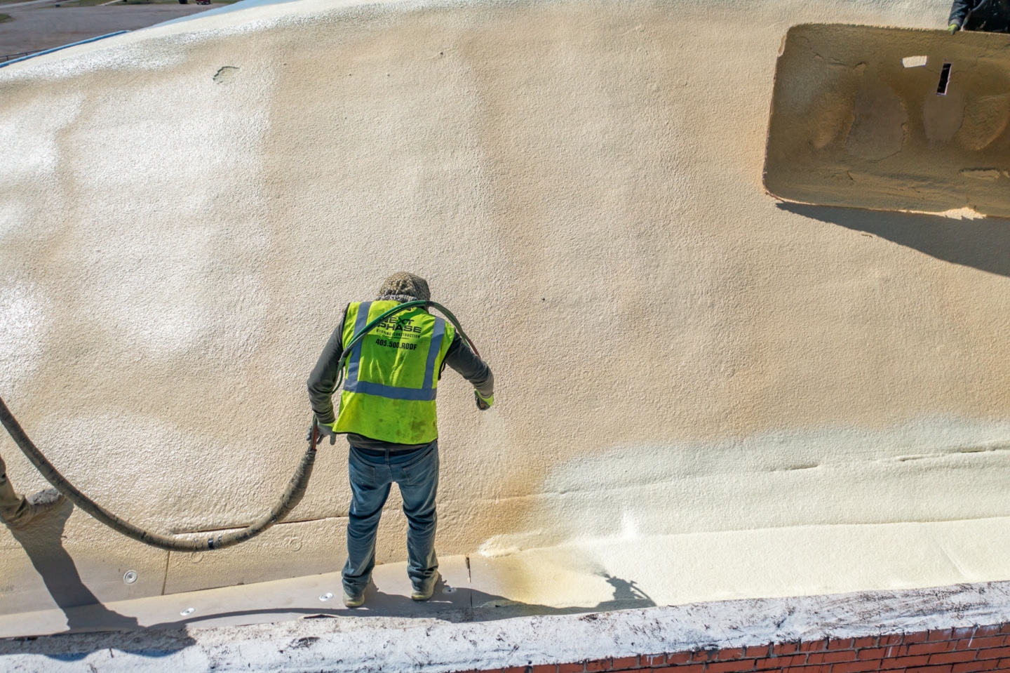 Worker spraying SPF roofing on a commercial building.