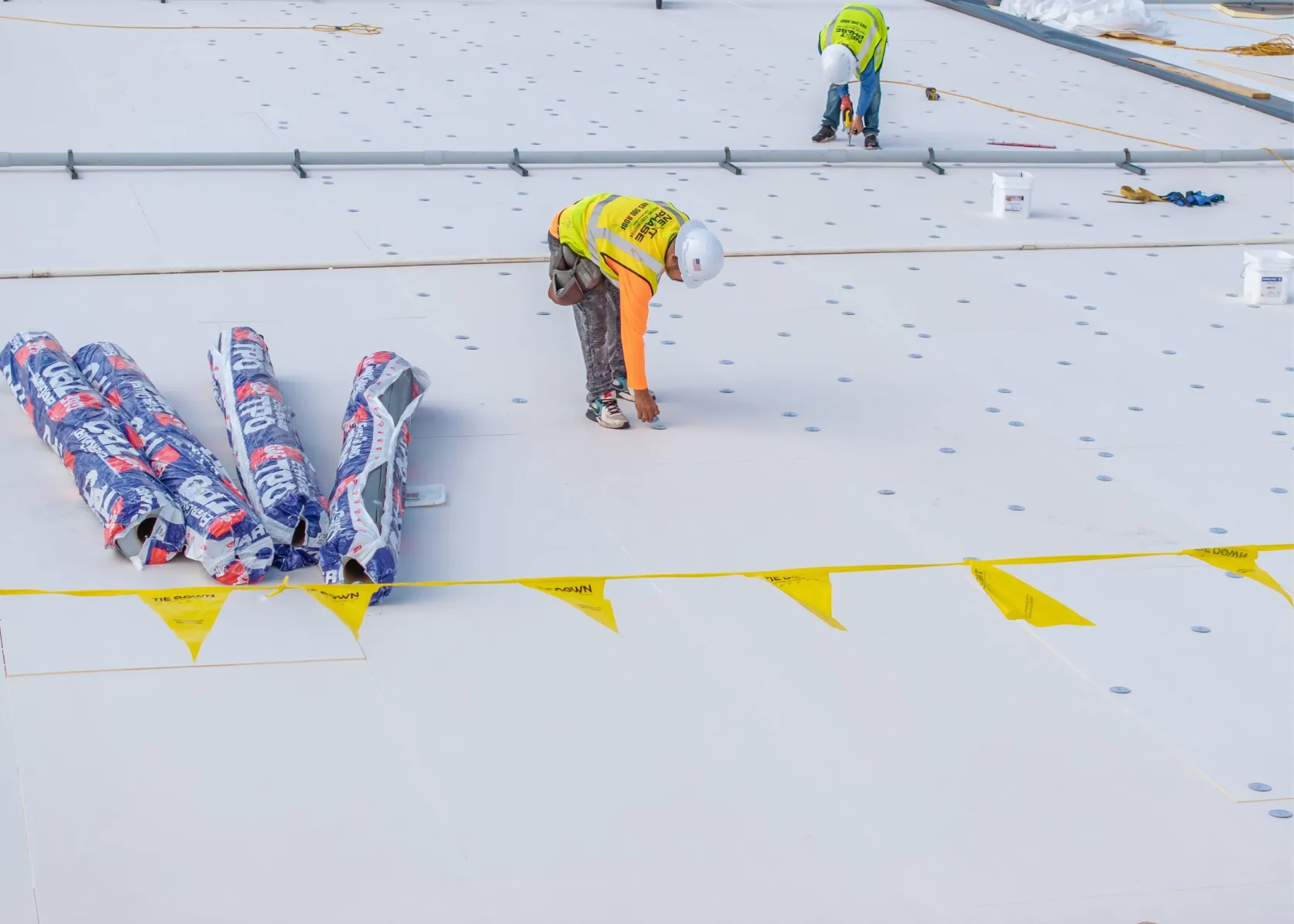 Crew installing white TPO membrane on flat commercial roo