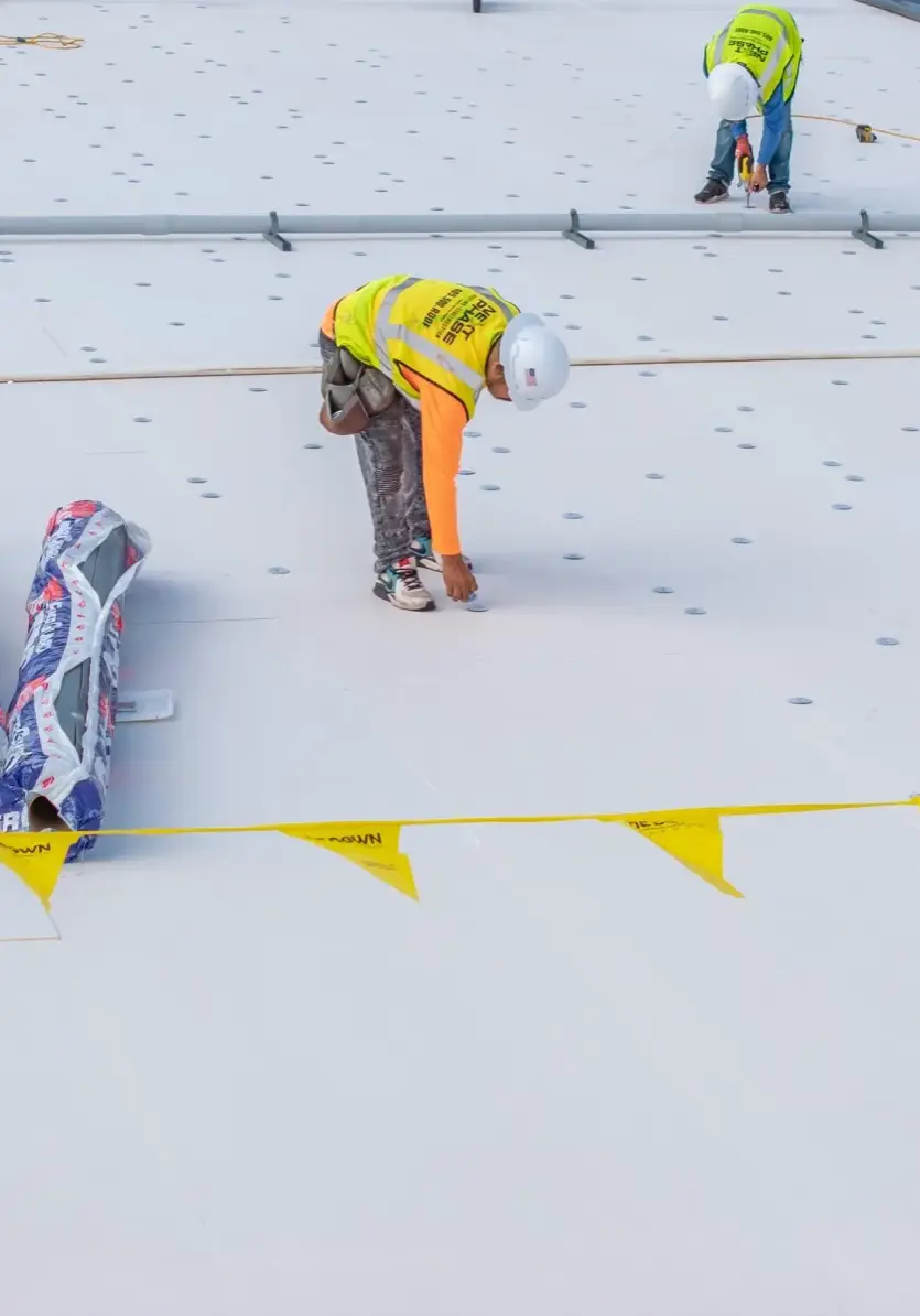 Crew installing white TPO membrane on flat commercial roo